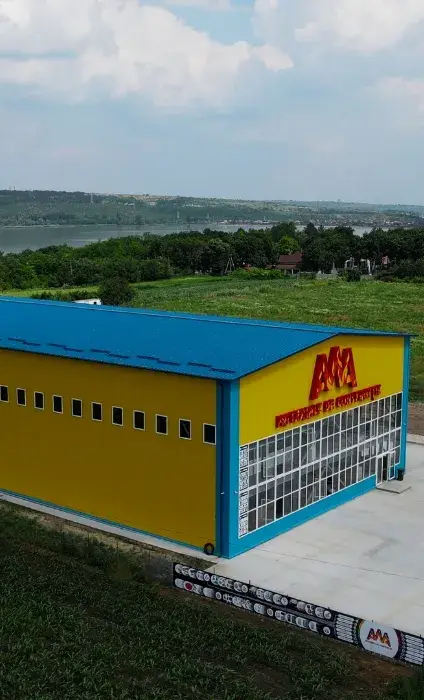 Hală metalică galbenă cu fațadă albastră, pe deal
